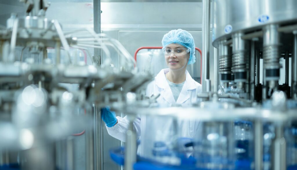 Female quality control worker inspecting water bottle on production line in drinking water factory