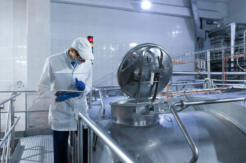 Inspector in a mask and a scrub stands with a folder-tablet in his hands at the dairy plant